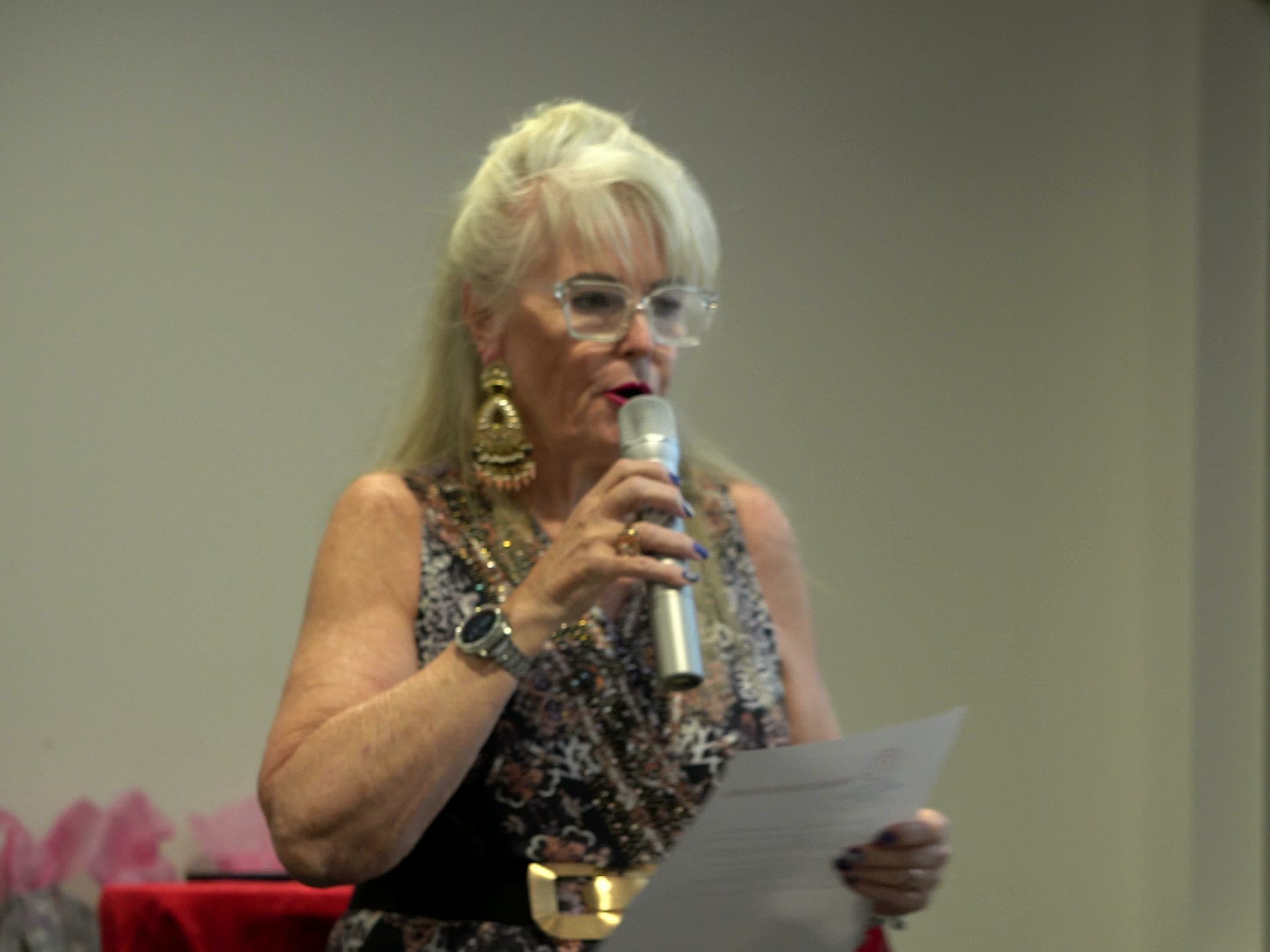Marion Simon, wearing glasses, speaking into a microphone and holding her notes during the welcome.