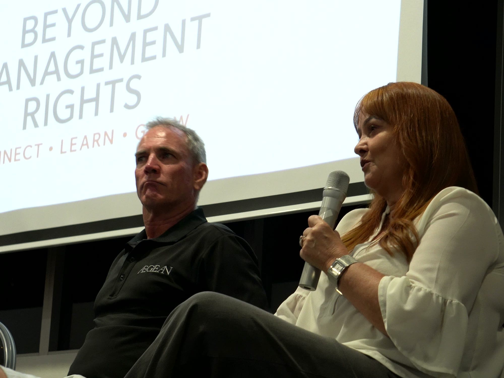 Two panellists seated in front of a Beyond Management Rights slide, one answering a question with a microphone.