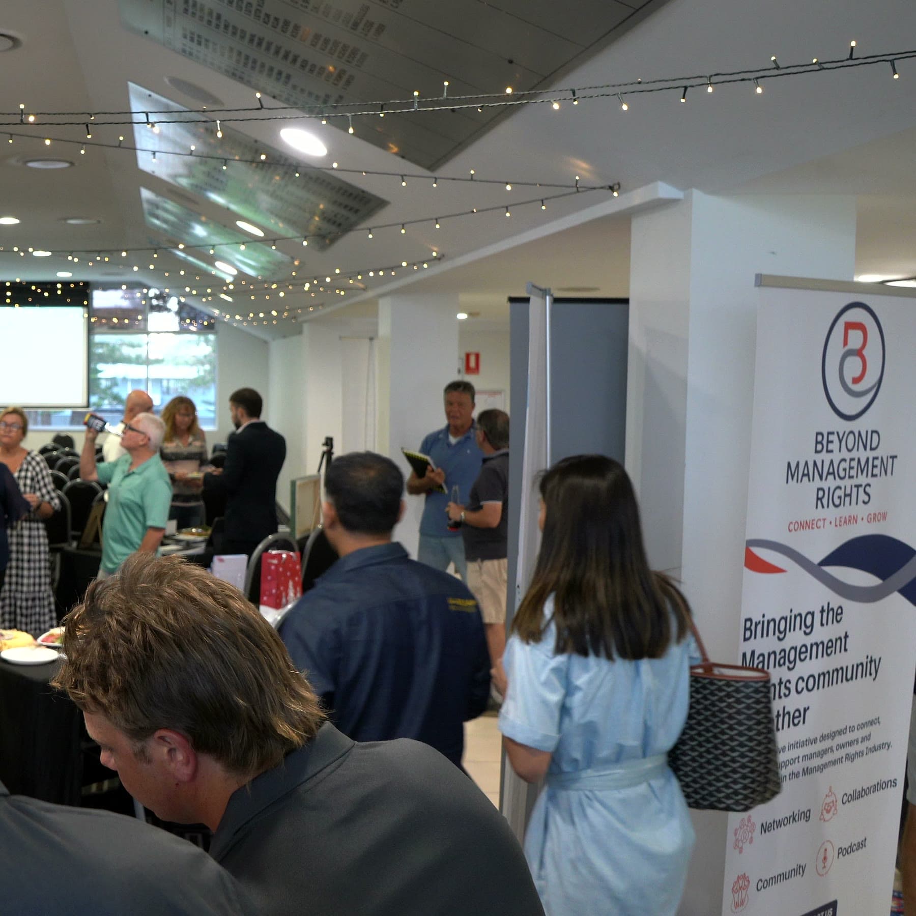 Guests networking in the function room at the inaugural Beyond Management Rights event, under festoon lights and beside a Beyond Management Rights banner.