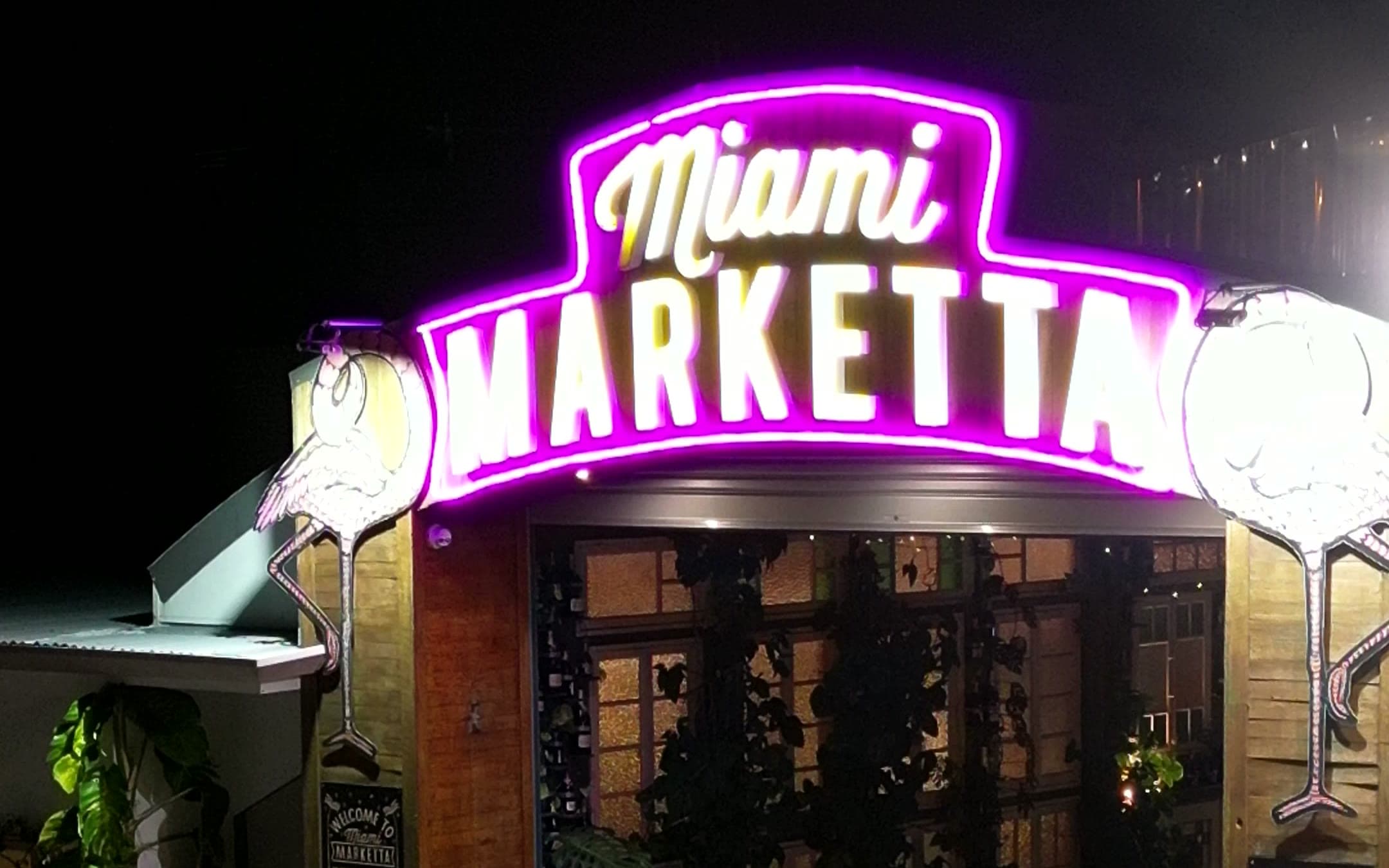 The lit Miami Marketta neon archway over the venue entrance at night.