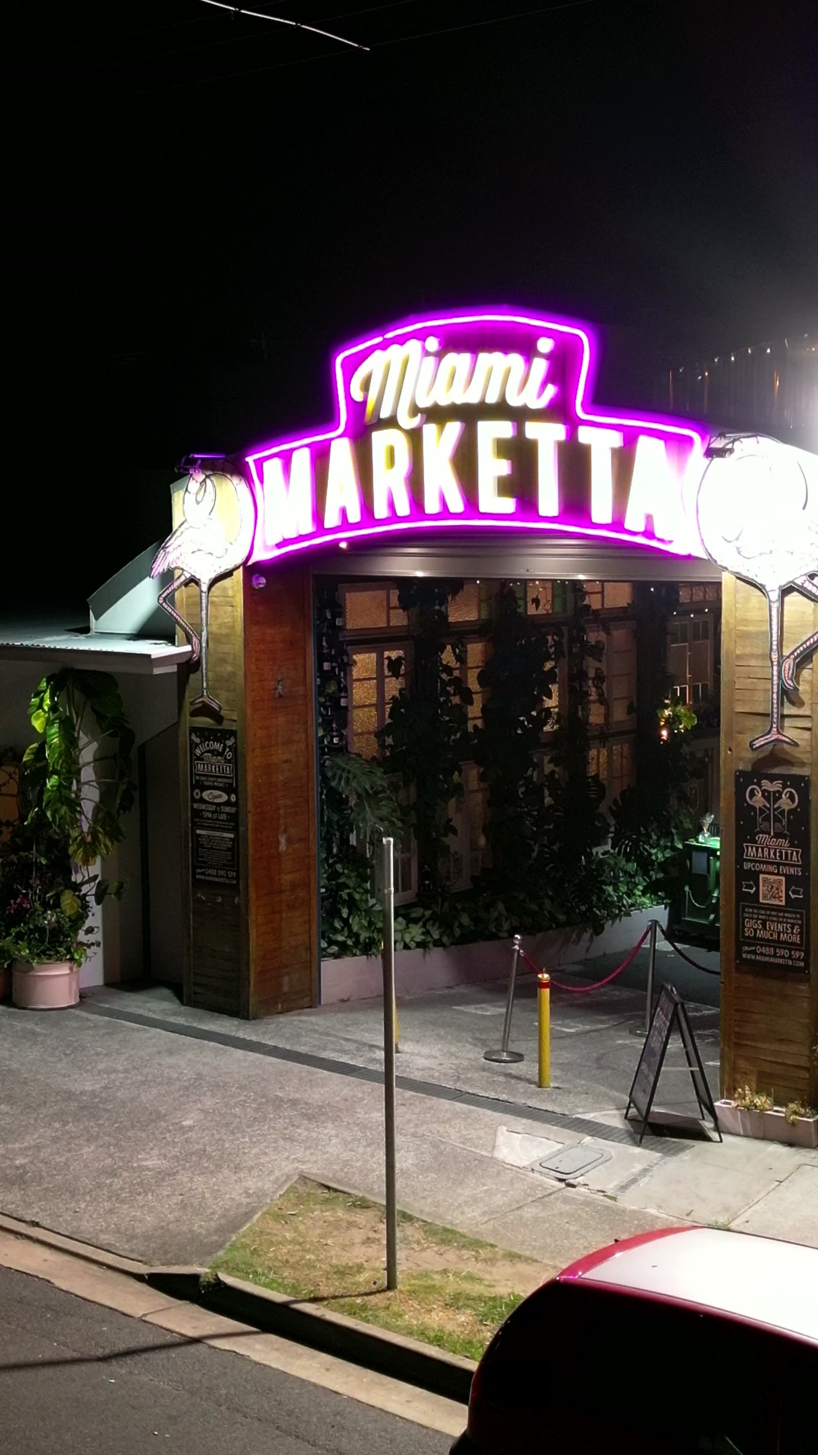 The lit Miami Marketta neon archway over the venue entrance at night.