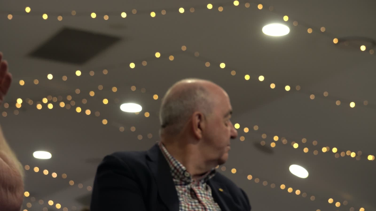 Strings of warm festoon lights across the function room ceiling above the seated guests.