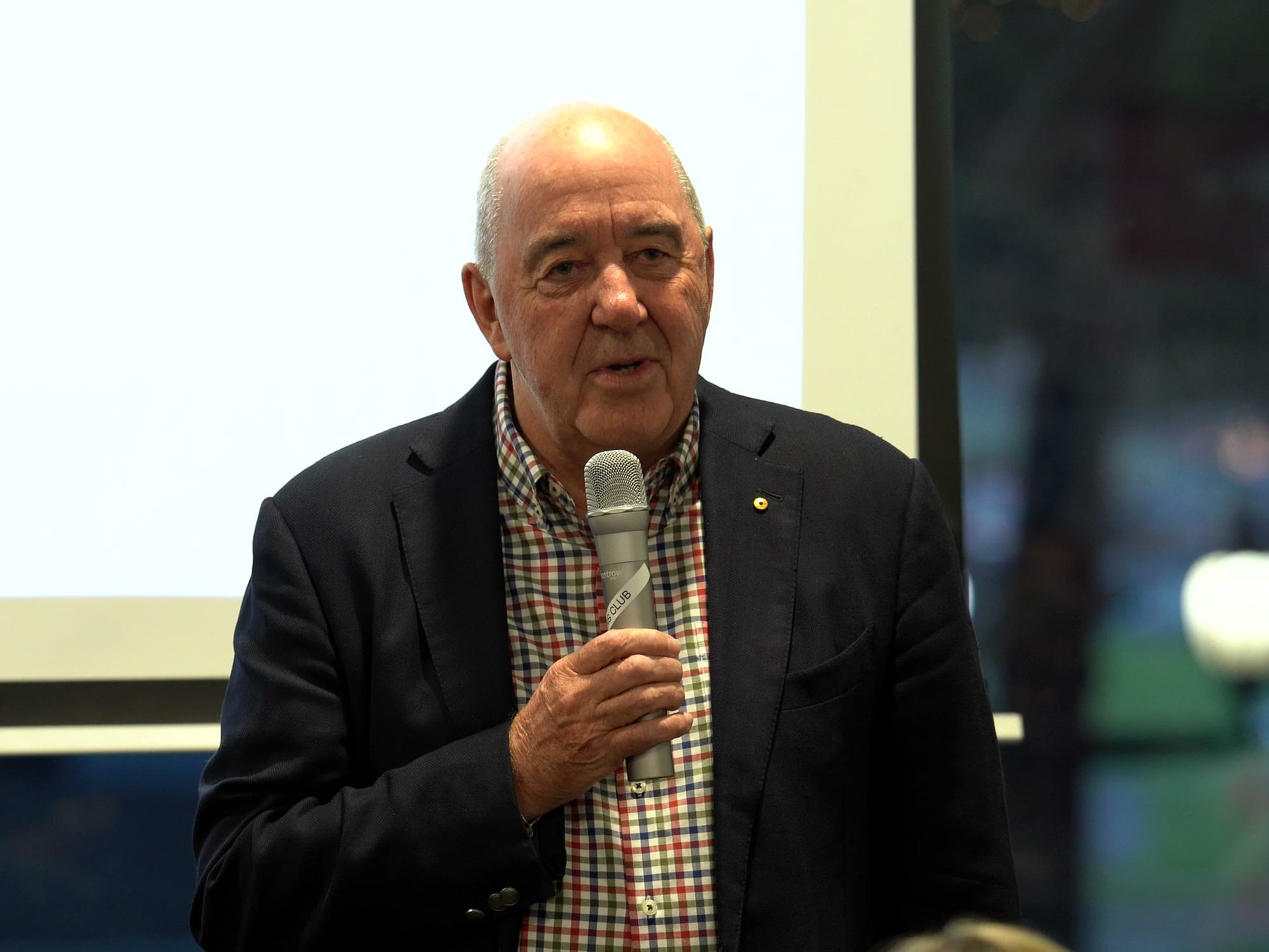 An industry speaker in a blazer addressing the room with a microphone.