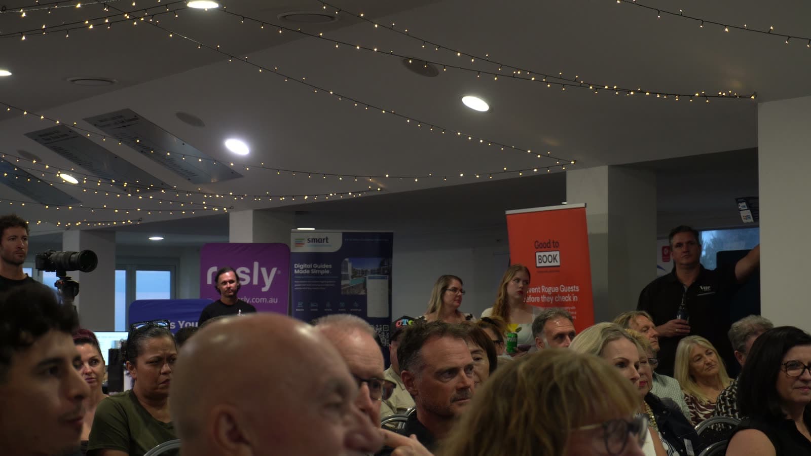 A full function room at the inaugural Beyond Management Rights event, with guests seated beneath festoon lights in front of exhibitor banners.