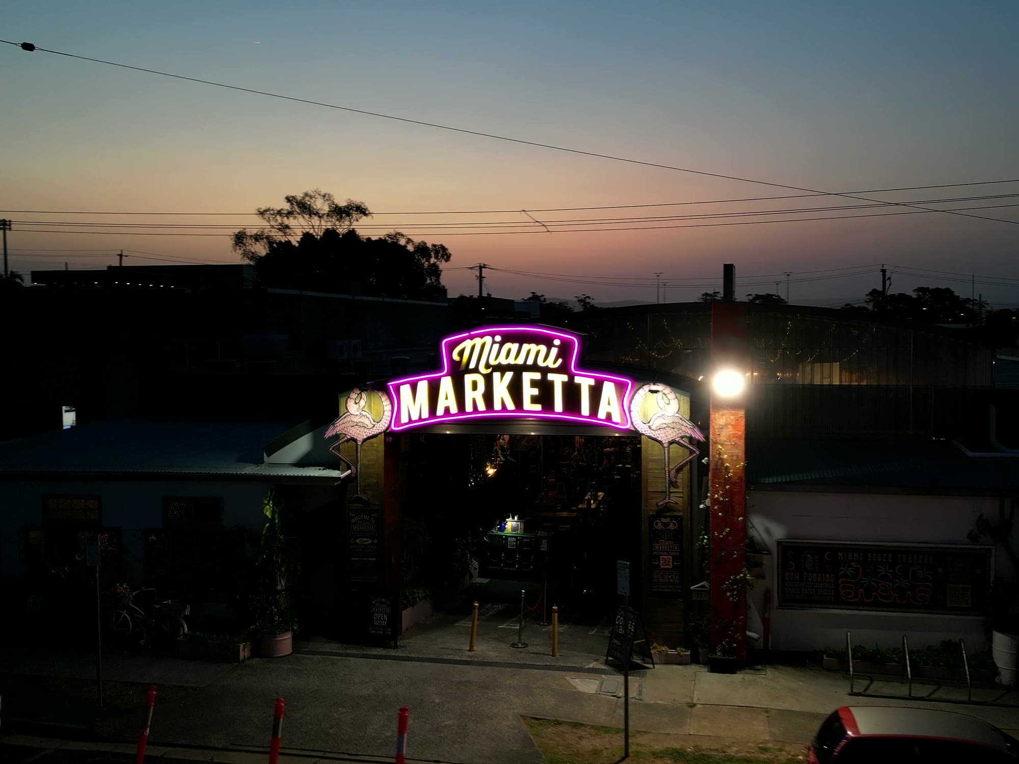 Miami Marketta's lit neon archway at dusk, seen from above the street with the sky still glowing.